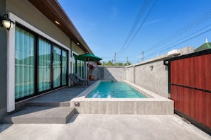 A swimming pool with a concrete deck, a covered seating area with chairs, and a red gate.