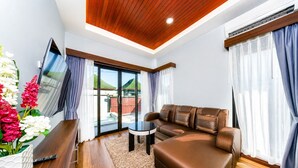 A modern living room with a sofa, a TV, a small table, and a large window with curtains. - Arterra Haven Aonang Krabi (Krabi)