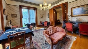 Um quarto com uma mesa de jantar, cadeiras, um sofá estofado, um piano e um candelabro.