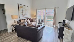 Ein Wohnzimmer mit einem dunklen Sofa, einem Couchtisch, einem Fernseher und einem Balkon mit Blick.