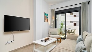 A modern living room with a flat-screen TV, a white coffee table, a sofa, and a sliding glass door leading to an outdoor area. - Apartment 'Building Copenhagen, Nerja' with Shared Pool, Wi-Fi and Air Conditioning (Nerja)