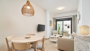 A modern living room with a round wooden table, two chairs, a sofa, a TV, and a large window. - Apartment 'Building Copenhagen, Nerja' with Shared Pool, Wi-Fi and Air Conditioning (Nerja)