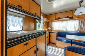 A compact RV interior with a kitchenette, a dining area, and a sleeping berth.