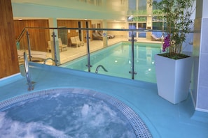 An indoor swimming pool with a glass balustrade, a hot tub, and lounge chairs. - Modern lodge on golf course with spa facilities (Blackawton)