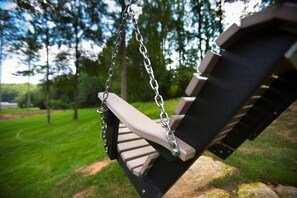 Une balançoire en bois avec des chaînes métalliques, installée devant un paysage verdoyant parsemé d’arbres.