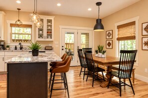 A kitchen with a marble island, wooden dining table, and chairs, with pendant lights and a view to the outside. - Family-Run, Super Clean Cottage 2 Miles from Asheville (Asheville)