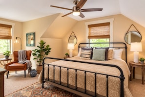 A bedroom with a bed, a chair, a ceiling fan, a window with a view, and a bedside table with a lamp. - Family-Run, Super Clean Cottage 2 Miles from Asheville (Asheville)