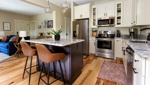 Una cocina moderna con armarios blancos, electrodomésticos de acero inoxidable y una isla central con taburetes de bar.