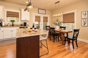 A kitchen with a central island, wooden dining table, and chairs. There are hanging lights, a clock, and framed artwork on the walls. - Immaculate Cottage, Clean Hot Tub, 2 Miles to Asheville (Asheville)