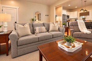 A living room with a grey sofa, a wooden coffee table, and a kitchen in the background. - Immaculate Cottage, Clean Hot Tub, 2 Miles to Asheville (Asheville)