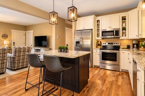 A modern kitchen with a central island, stainless steel appliances, and a dining area with plaid chairs. - Exceptionally Clean Cottage with Private Hot Tub Near Asheville (Asheville)