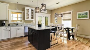 A kitchen with a central island, white cabinetry, and a dining area with a table and chairs. - Exceptionally Clean Cottage with Private Hot Tub Near Asheville (Asheville)