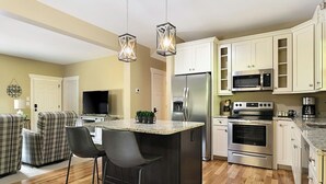A modern kitchen with a central island, stainless steel appliances, and a dining area with a TV and seating. - Exceptionally Clean Cottage with Private Hot Tub Near Asheville (Asheville)
