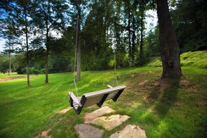 A wooden swing suspended by chains, set in a grassy area with trees in the background. - Exceptionally Clean Cottage with Private Hot Tub Near Asheville (Asheville)