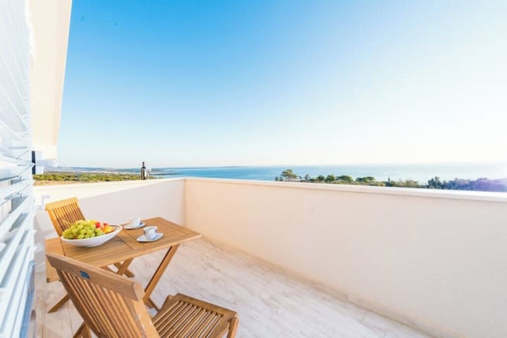 Un balcone con tavolo e sedie, una ciotola di frutta e vista libera sul mare.