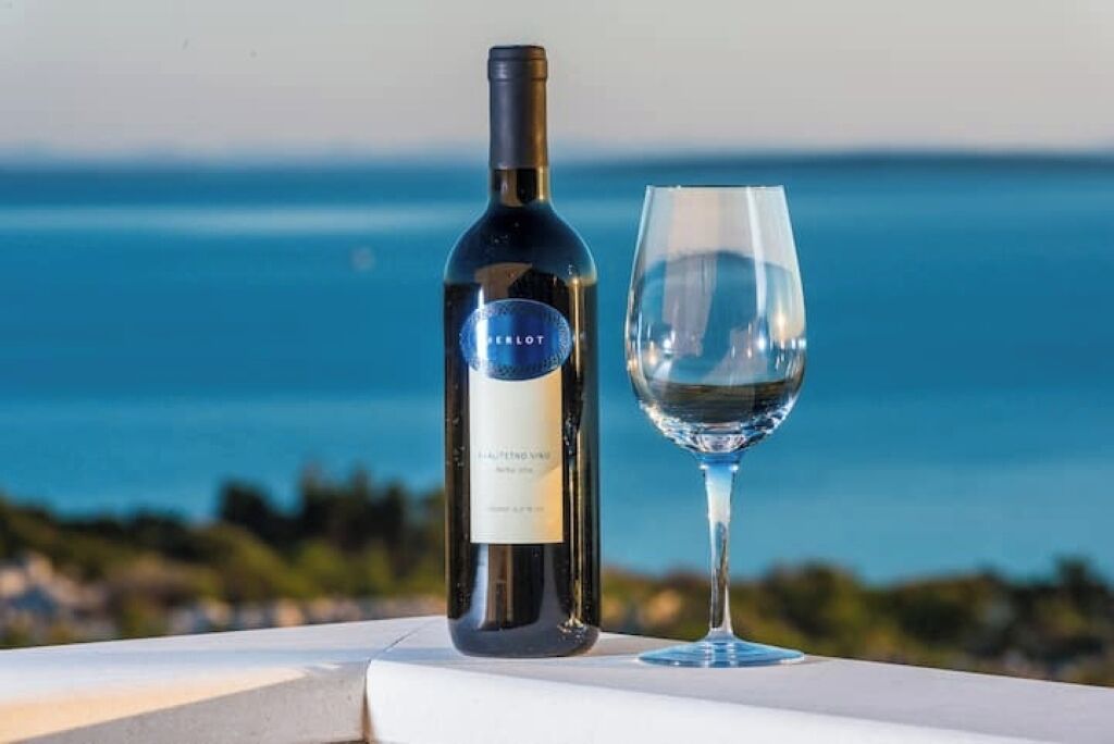Una botella de vino y una copa en un balcón con vistas al mar.