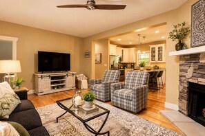 A modern living room with a flat-screen TV, plaid armchairs, a coffee table, and a fireplace. - Immaculate Cottage with Private Hot Tub and Fireplace (Asheville)
