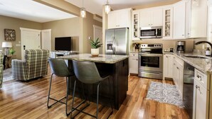 A modern kitchen with white cabinets, stainless steel appliances, and a central island with bar stools. - Immaculate Cottage with Private Hot Tub and Fireplace (Asheville)