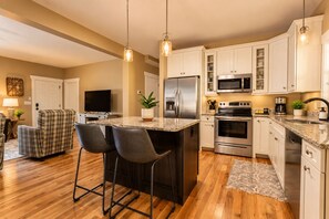 A modern kitchen with a central island, stainless steel appliances, and a seating area with a television and bar stools. - Immaculate Cottage with Private Hot Tub and Fireplace (Asheville)