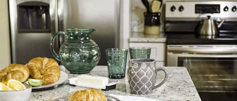 A kitchen with a refrigerator, microwave, and stove. There are croissants on a plate, a pitcher, and a mug on the counter.