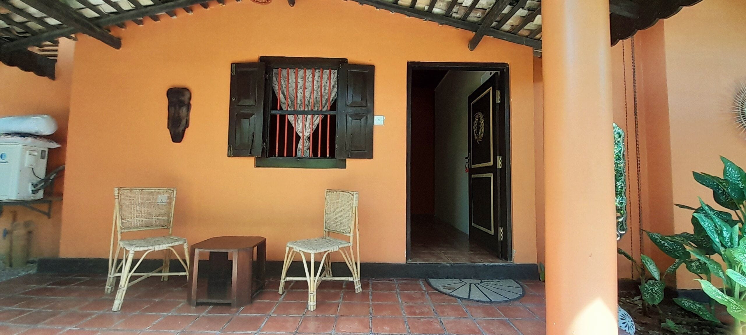 Un espacio al aire libre cubierto con dos sillas de mimbre, una mesita y una puerta que da al interior.