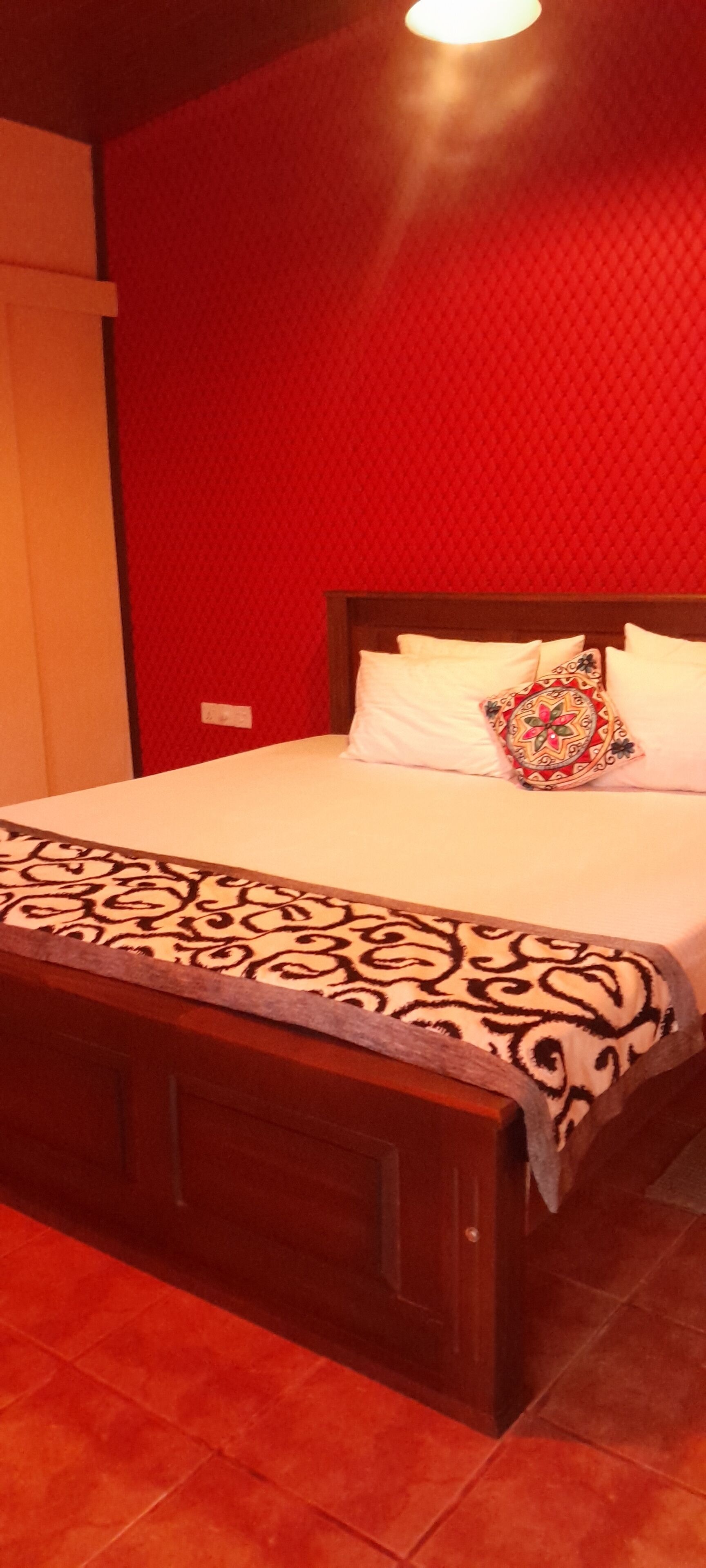 Une chambre avec un lit, un plaid à motifs et un mur rouge.