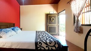 A bedroom with a bed, a headboard, a door with a wreath, and a window with curtains. - The Fat Mermaid (Mirissa)