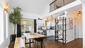 A modern kitchen with white cabinets, a wooden dining table, and a black metal shelving unit. - 4BR Retreat with Jacuzzi & Mont-Tremblant View (Mont-Tremblant)