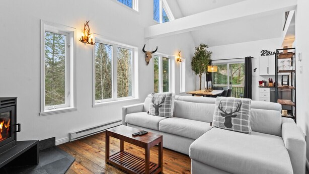 A modern living room with a fireplace, large windows, and a cozy seating area. - 4BR Retreat with Jacuzzi & Mont-Tremblant View (Mont-Tremblant)