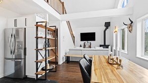 A modern kitchen with a built-in refrigerator, wooden shelves, a dining table with candles, and a staircase leading to an upper level. - 4BR Retreat with Jacuzzi & Mont-Tremblant View (Mont-Tremblant)