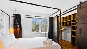 A modern bedroom with a four-poster bed, a large window with a view of trees, and a wooden wardrobe with a sliding door. - 4BR Retreat with Jacuzzi & Mont-Tremblant View (Mont-Tremblant)