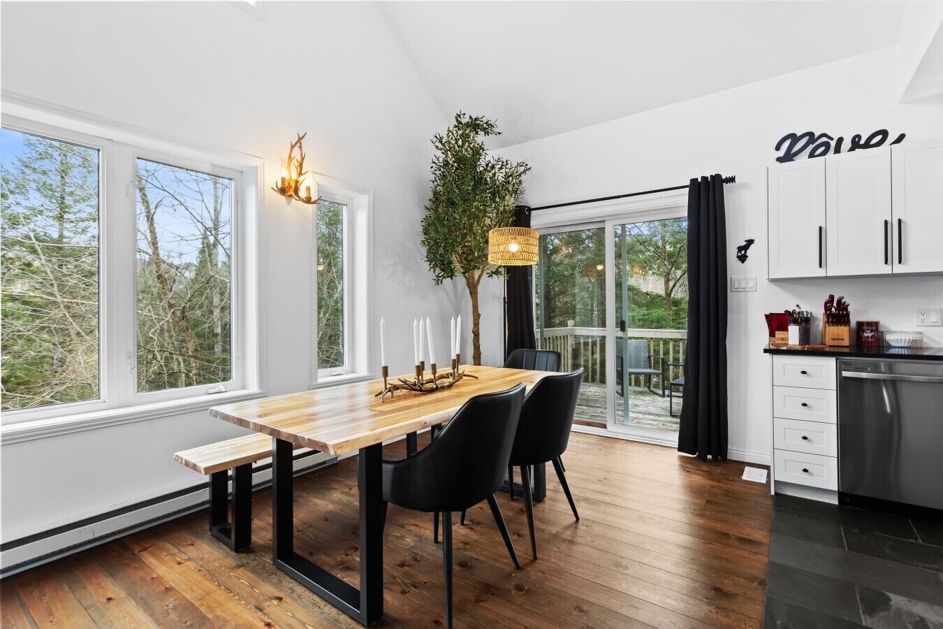 Una cucina moderna con un tavolo da pranzo in legno, sedie nere e un'ampia finestra con vista sugli alberi.