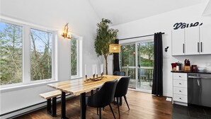 A modern kitchen with a wooden dining table, black chairs, and a large window offering a view of trees. - 4BR Retreat with Jacuzzi & Mont-Tremblant View (Mont-Tremblant)