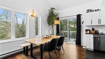 Una cucina moderna con un tavolo da pranzo in legno, sedie nere e un'ampia finestra con vista sugli alberi.