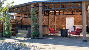An outdoor patio area with a covered seating area, a fire pit, and a staircase leading to an upper level. - Serene coastal ambiance, fenced yard, fire pit, and outdoor furniture! (Seaside)