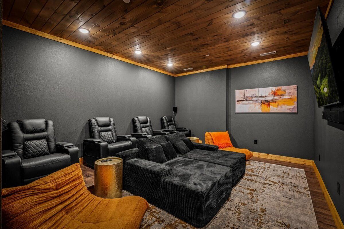 Une salle de cinéma privée avec des murs gris foncé, un plafond en bois et des sièges en cuir noir.