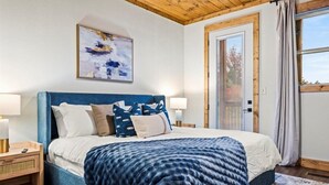 A bedroom with a large bed, a wooden headboard, a painting above the bed, a nightstand with a lamp, and a window with curtains. - *Luxurious 6BD Lodge w/ POOL | Hot Tub + Theater* (Sevierville)