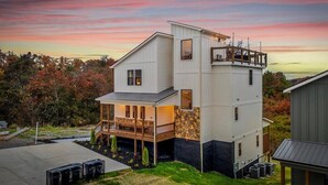 A modern two-story house with a deck and a stone foundation. - *Luxurious 6BD Lodge w/ POOL | Hot Tub + Theater* (Sevierville)