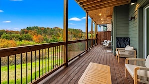 Terraza de madera con vistas a follaje otoñal, chimenea de piedra y mobiliario exterior.