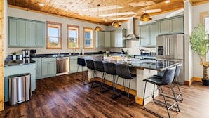 Una cocina amplia con vigas de madera en el techo, armarios verde claro y electrodomésticos de acero inoxidable, además de una isla central con taburetes de bar.