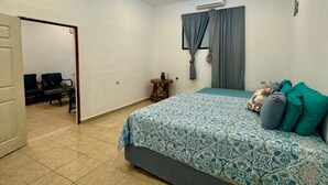 Une chambre à coucher comprenant un lit, une chaise, une petite table et une porte donnant sur une autre pièce.