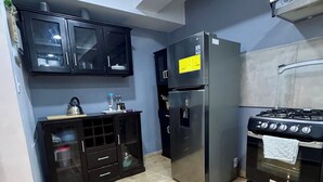 Une cuisine de taille réduite avec des meubles noirs, un réfrigérateur en acier inoxydable, une cuisinière à gaz et un sol carrelé.