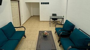 Un salon avec deux canapés de couleur turquoise, une table basse ornée d’un vase de fleurs, une petite table avec une chaise et une porte.