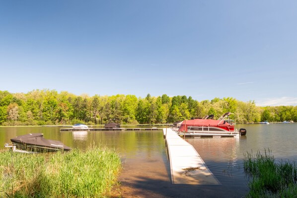 A calm lake with docked boats, a red boat with a canopy, and a small building on the shore. - Lakefront w Dock, Pool, & Courts (Oakland)