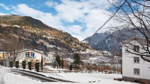 A snow-covered landscape with a mountain, a residential area, and a building with a balcony.