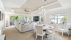 A spacious living room with a large sofa, dining table, and chairs, a ceiling fan, and large windows with a view of greenery. - JUST LISTED! Heaven On Earth! Dis/Reunion. Gorgeous, Spacious, 8 Pools, Slps 10 (Kissimmee)