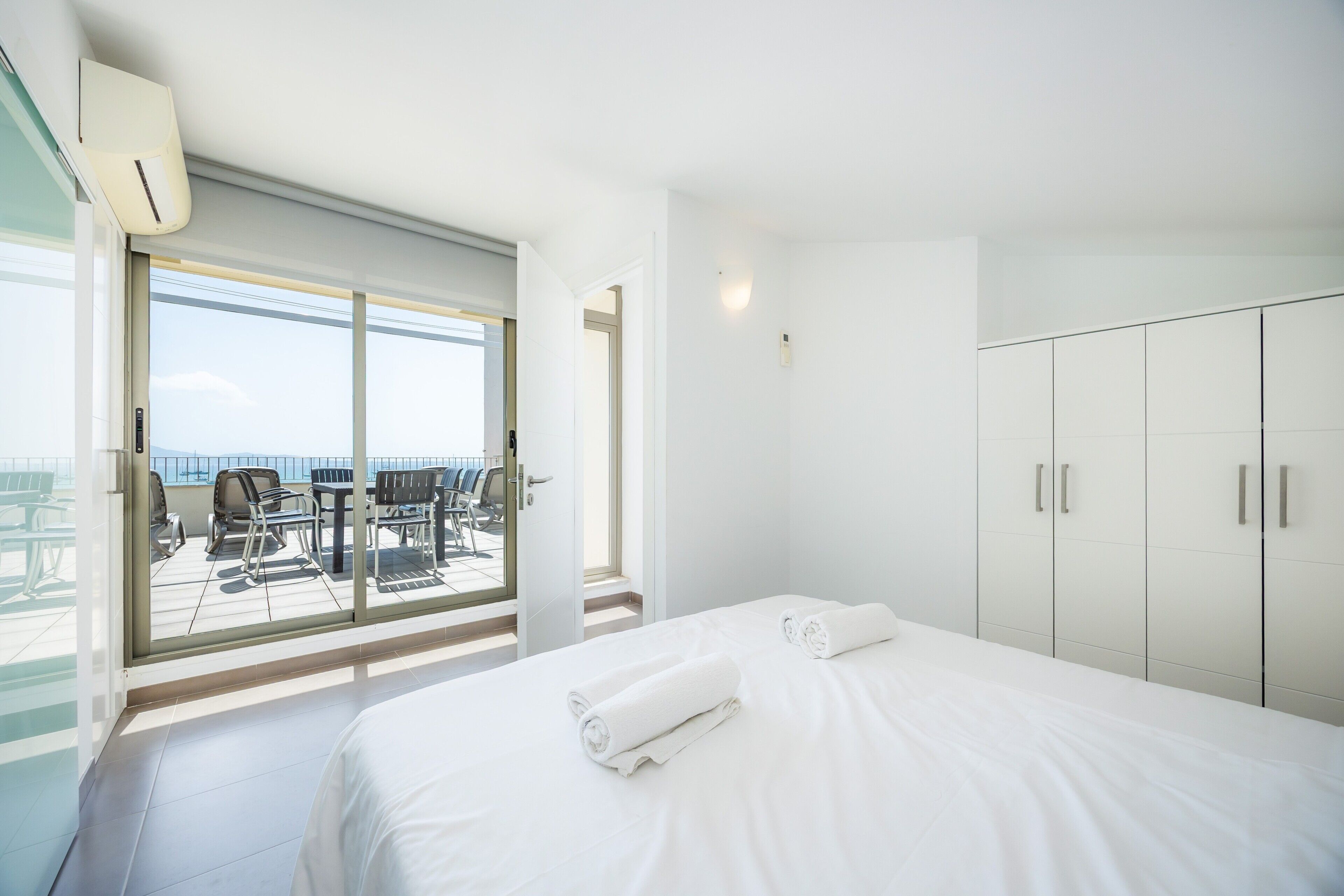 A hotel room with a bed, a balcony with chairs, and a view of the sea.