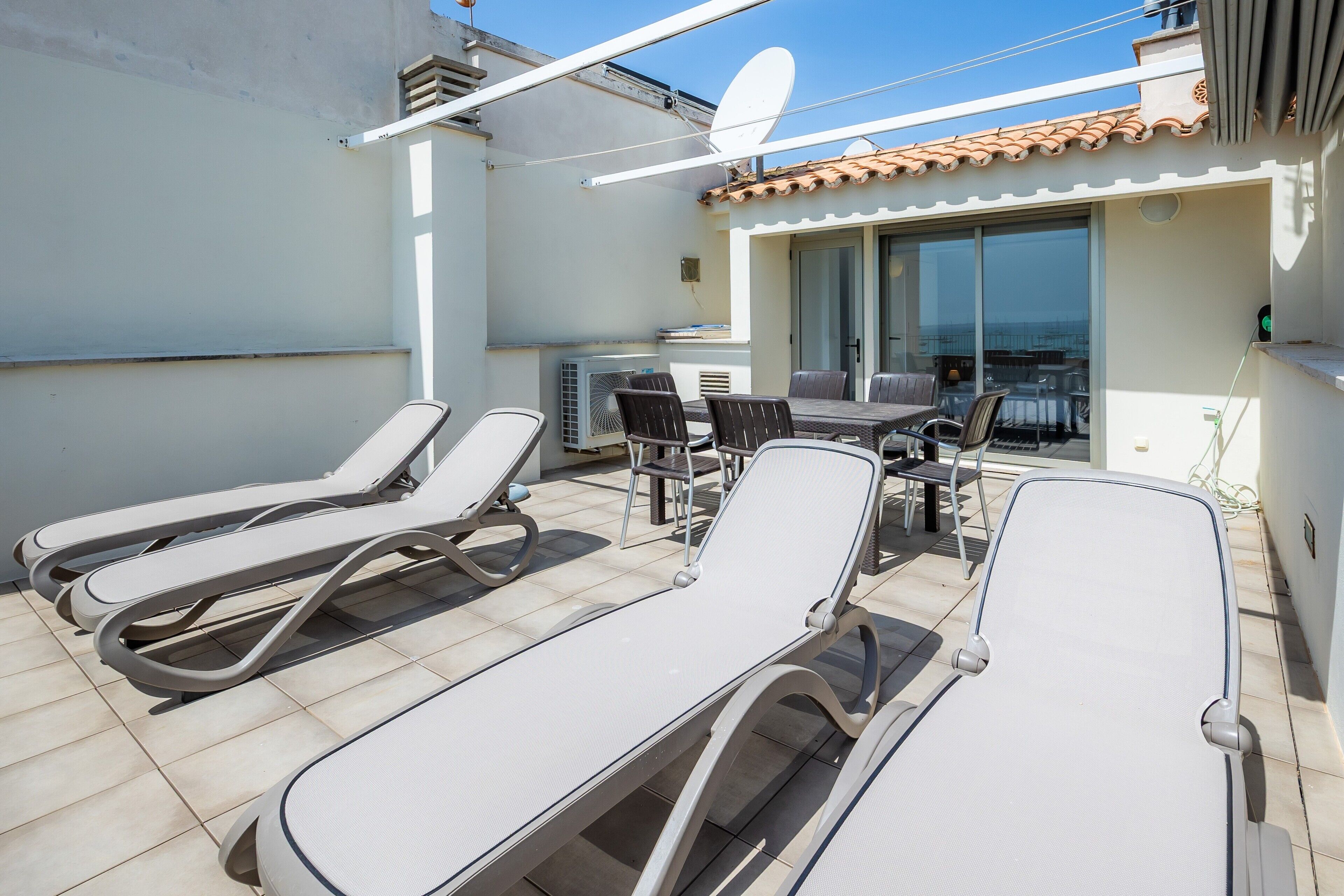 Eine Dachterrasse mit Liegestühlen, einem Tisch und Blick aufs Meer.