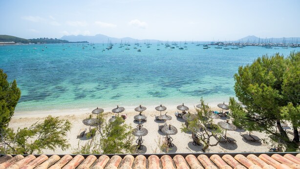 Une plage avec une eau turquoise et limpide, de nombreux voiliers et des parasols de plage.