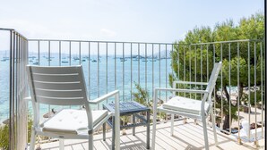 Un balcon avec deux chaises blanches et une petite table, donnant sur une marina où sont amarrés des bateaux.